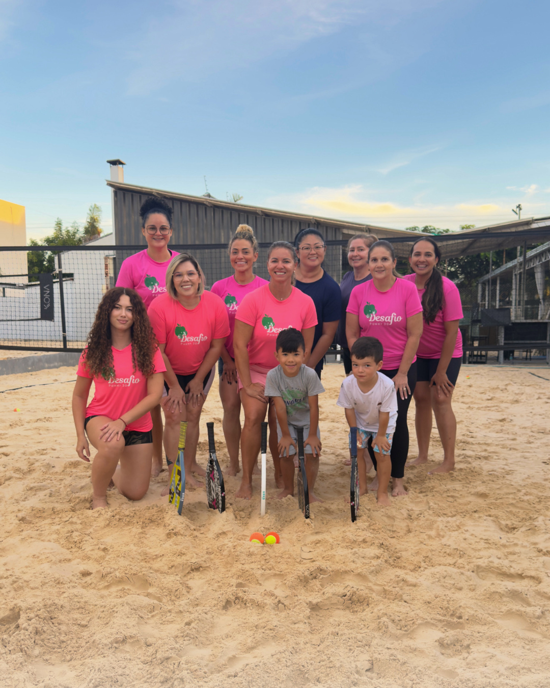 Grupo do Desafio Power 30 com camisetas rosa em uma quadra de beach tennis